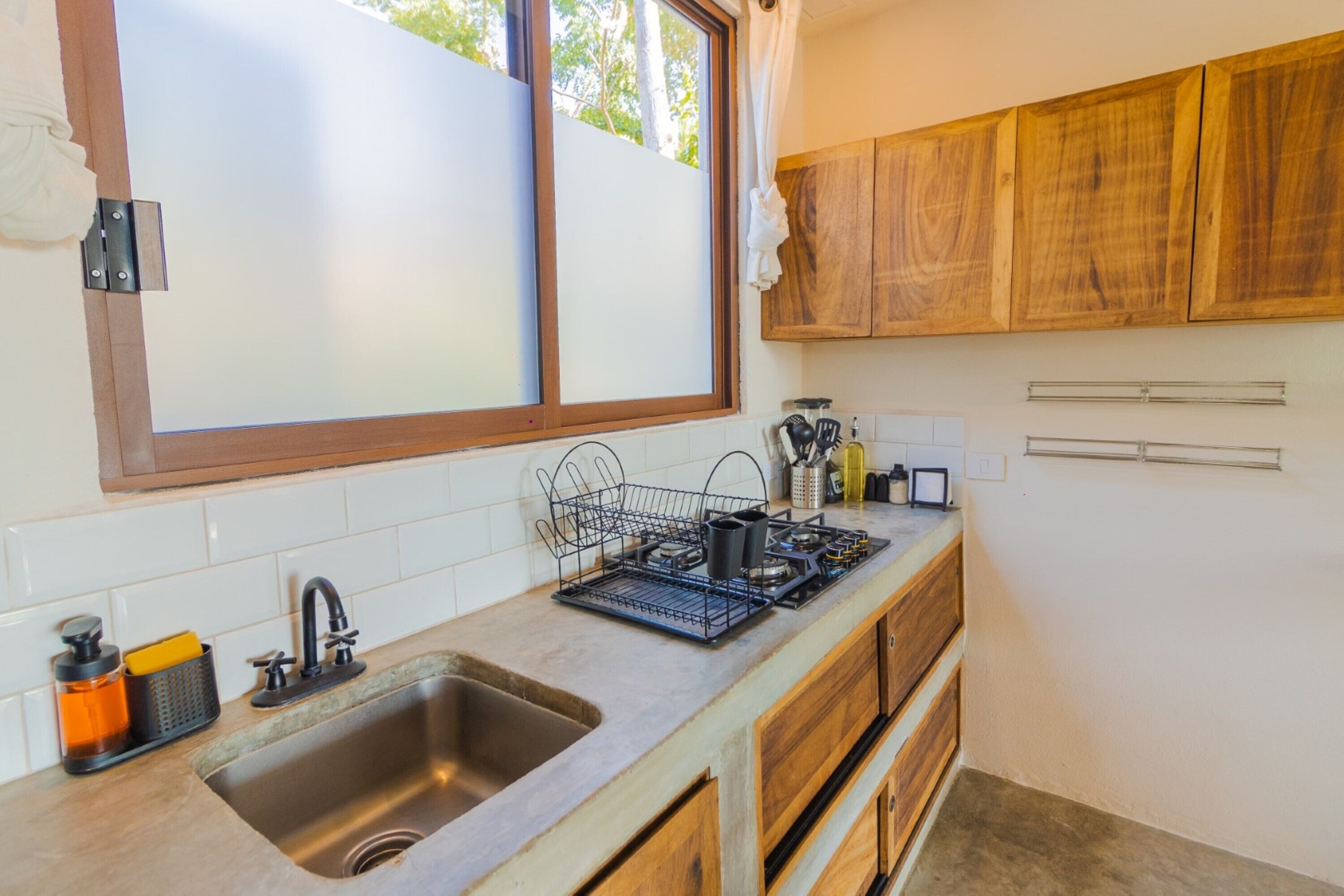 A kitchen with a large window, wooden cabinets, a stainless steel sink, and a dish rack.