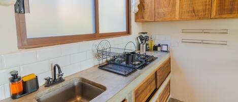 A kitchen with a large window, wooden cabinets, a stainless steel sink, and a dish rack.
