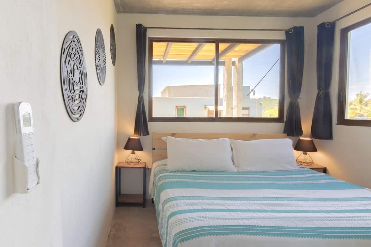 Un dormitorio con cama, dos mesitas de noche, una ventana con cortinas y decoración en la pared.