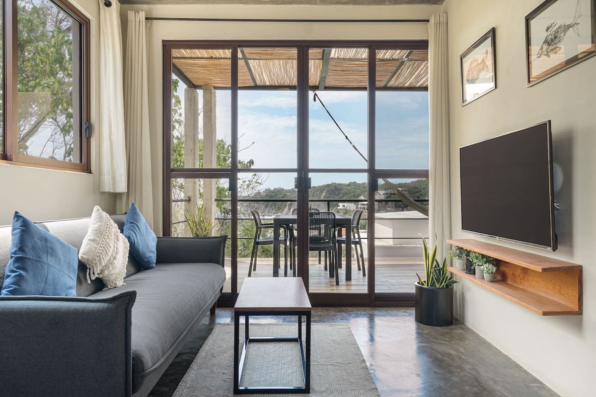 Una sala de estar moderna con un sofá, una mesa de centro, un televisor y un balcón con vistas.