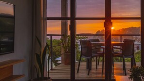 Une chambre moderne dotée de grandes portes-fenêtres coulissantes qui donnent sur une terrasse extérieure offrant une vue sur le coucher de soleil et un paysage montagneux.