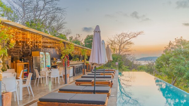 Un espace aménagé au bord de la piscine, avec des chaises longues, des parasols et un bar doté de tables en plein air.