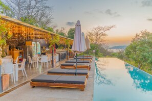 A poolside area with lounge chairs, umbrellas, and a bar with outdoor seating.