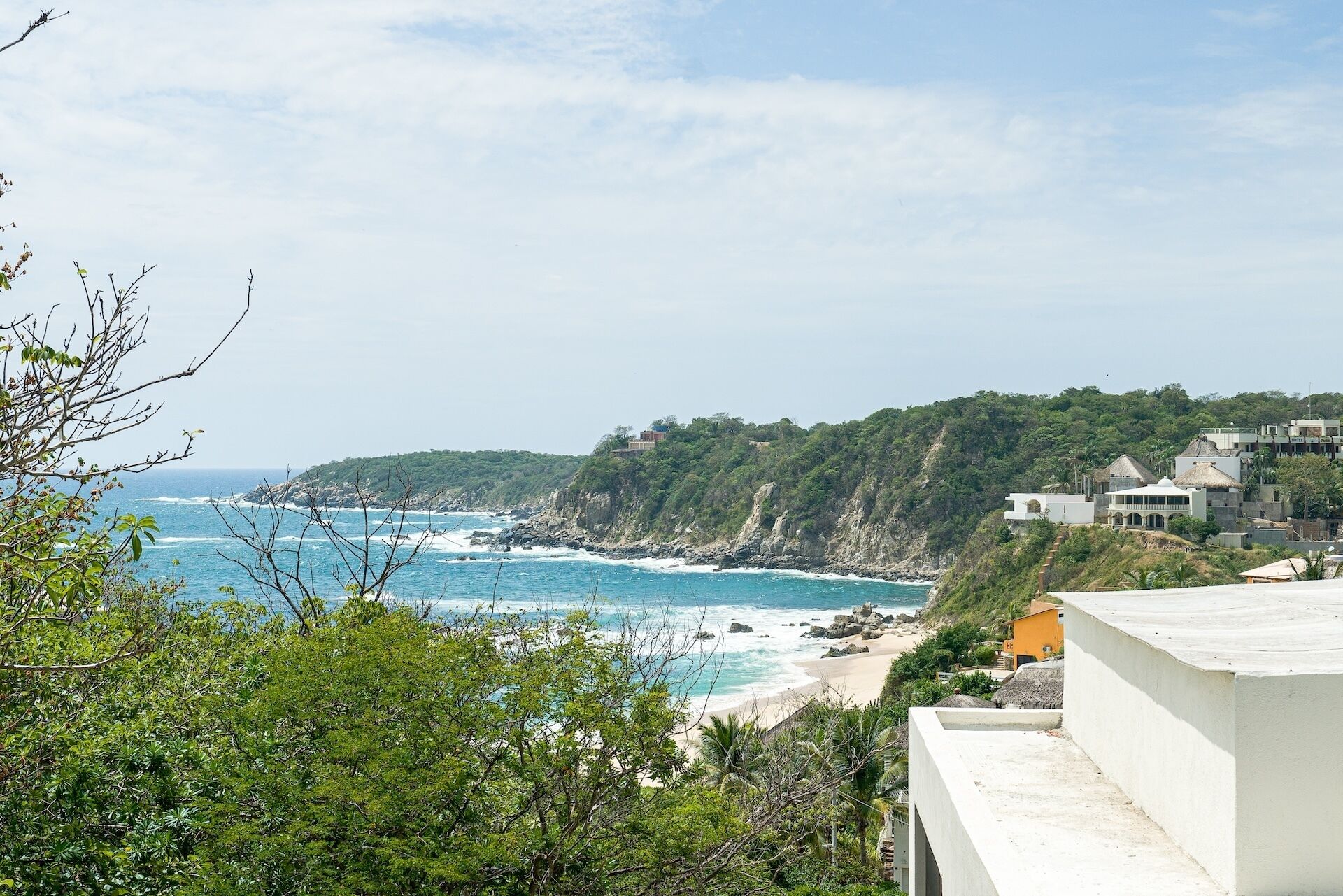 A coastal view with a beach, rocky cliffs, and buildings.