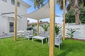 Een terras met witte meubels, een groot wit huis en een houten omheining.