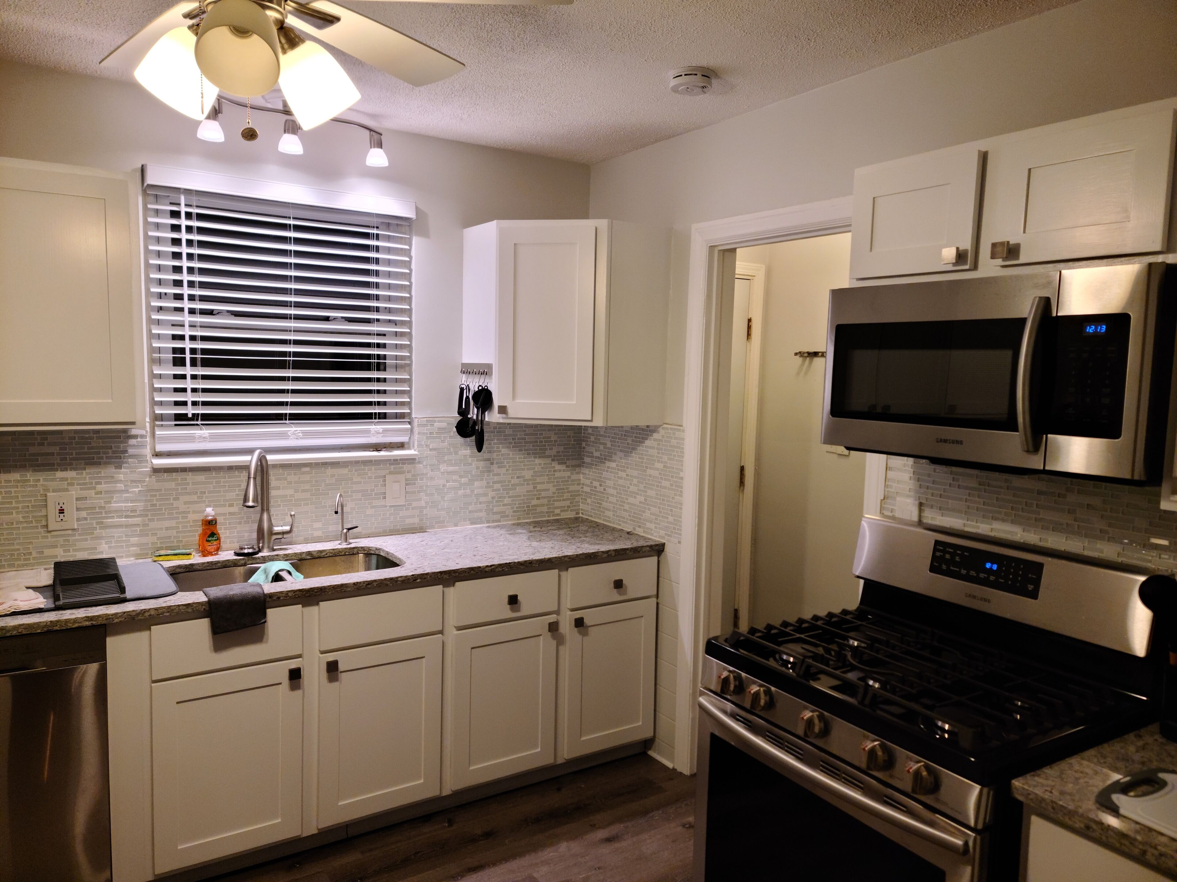 Una cocina con armarios blancos, un lavaplatos de acero inoxidable, un microondas y una estufa.