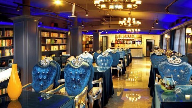 A library with rows of blue velvet chairs and tables, a chandelier, and bookshelves. - Tianlong Hotel (Zibo)