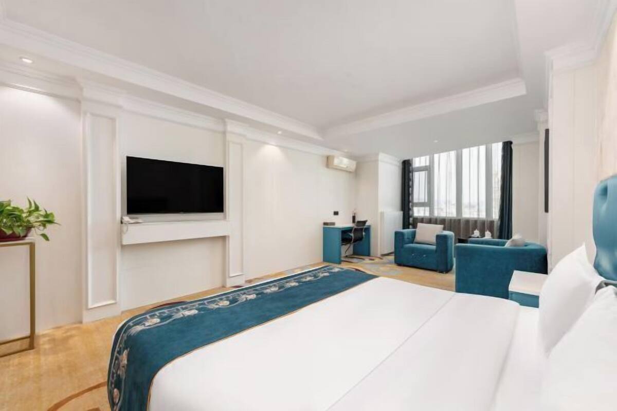 A hotel room with a large bed, a TV mounted on the wall, a desk with a chair, and a sofa.