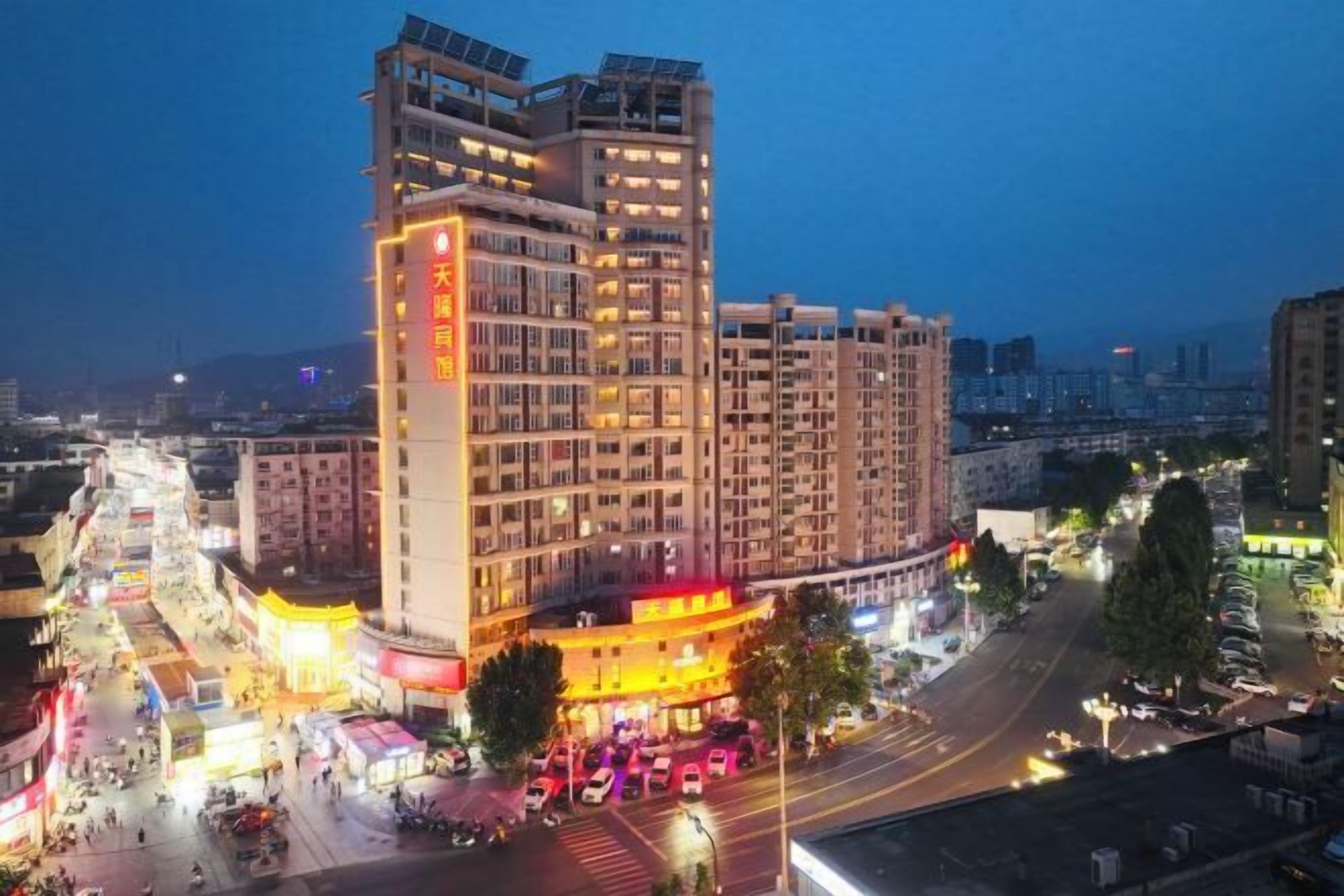 Un hotel de varios pisos con un edificio destacado en esquina, un estacionamiento y una calle con vehículos.
