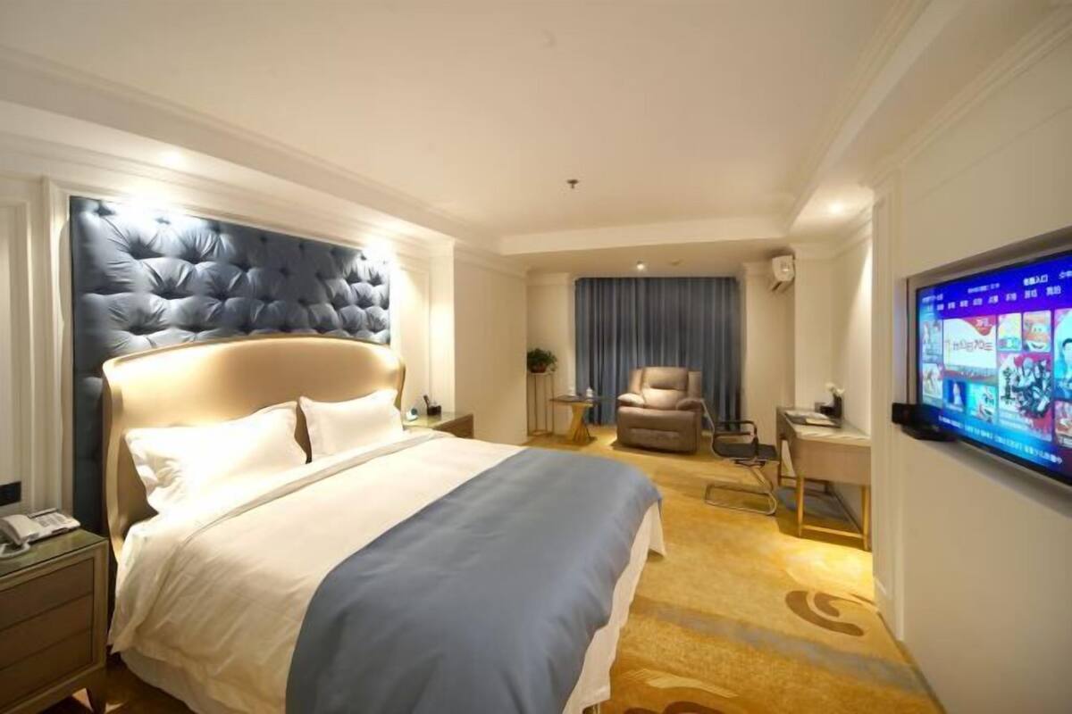 A hotel room with a large bed, a television, a desk, and a chair.