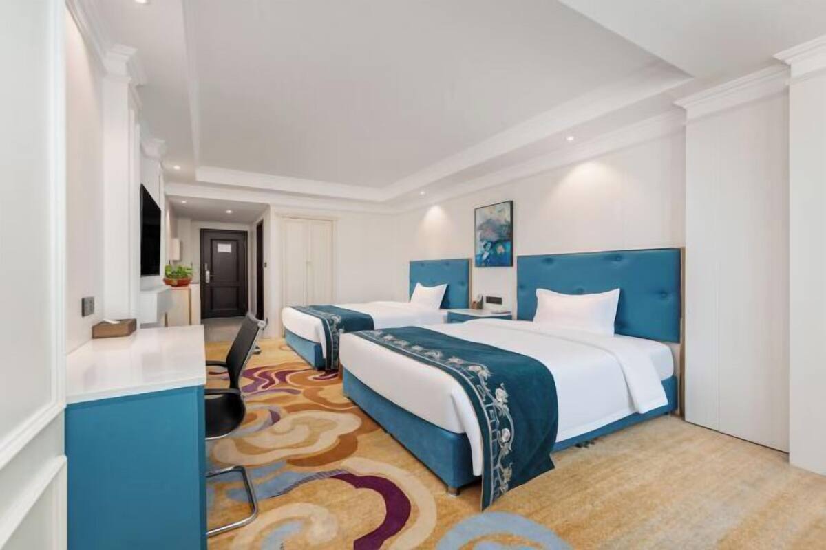 A hotel room with two beds, a desk, a chair, and a patterned carpet.