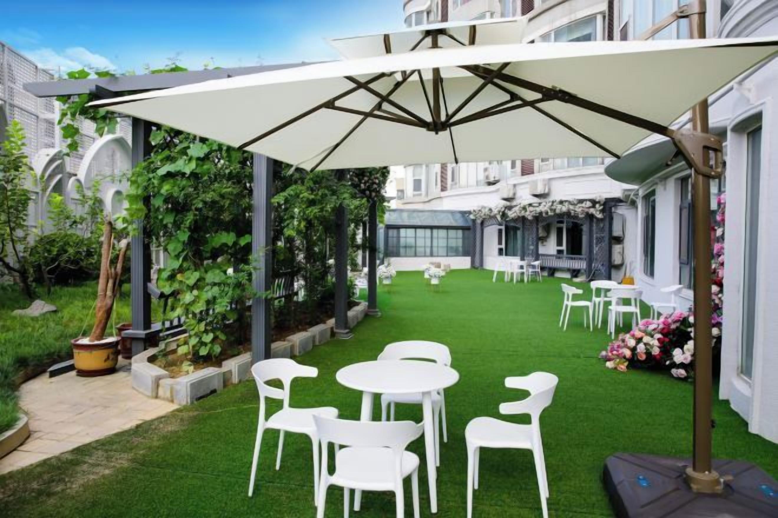 Un patio con una sombrilla blanca, sillas blancas y césped verde.