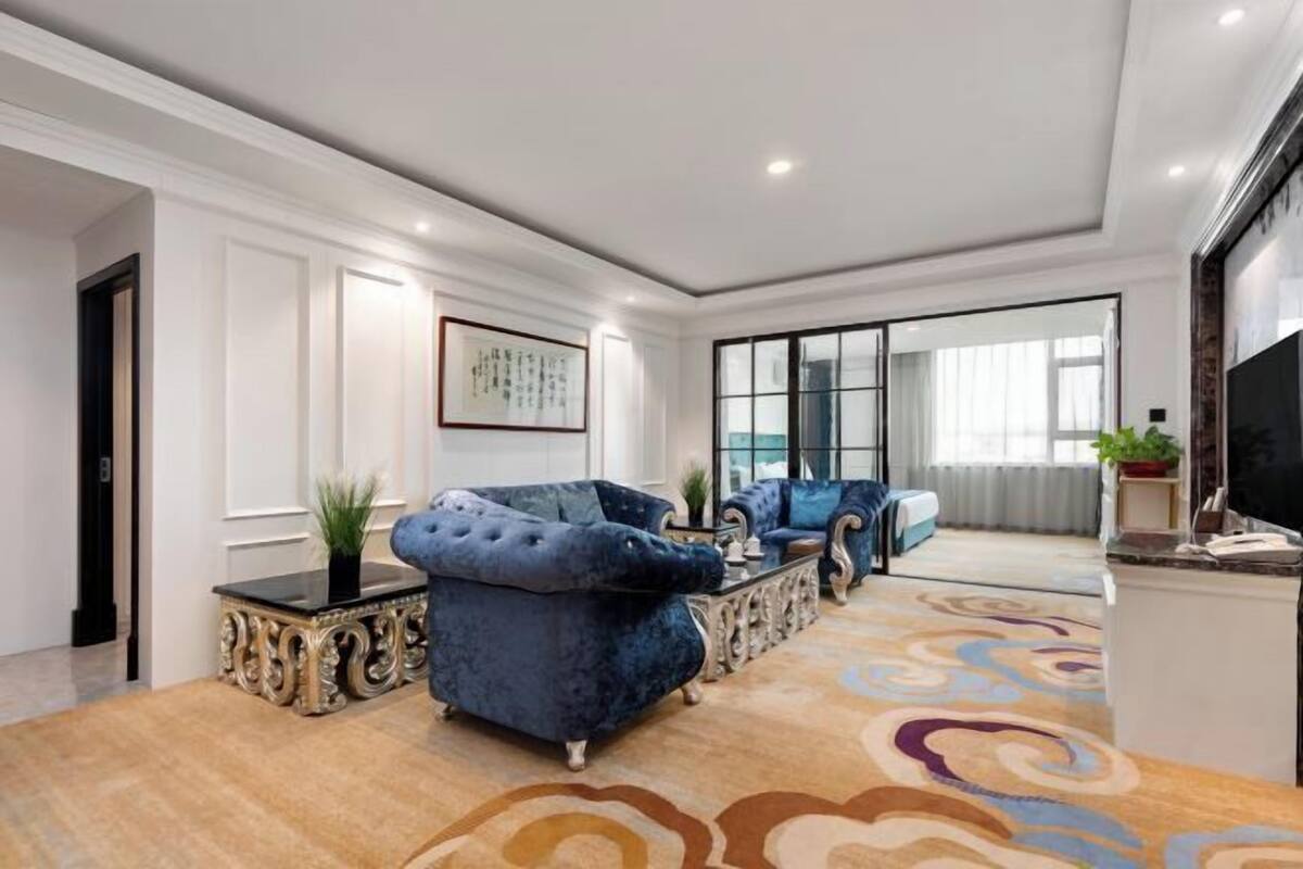 A spacious living room with a large window, a blue sofa, a coffee table, and a patterned carpet.