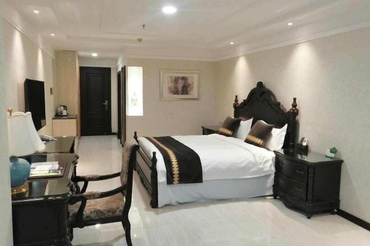 A hotel room with a large bed, a desk with a lamp, a chair, and a dresser.