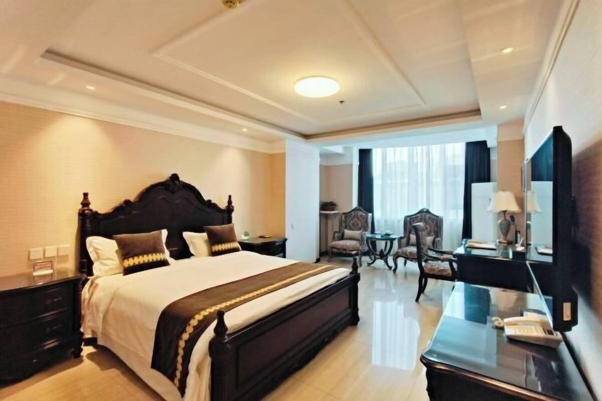 A hotel room with a large bed, a desk, a chair, and a mirror.