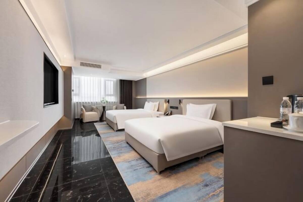 A modern hotel room with two beds, a flat-screen TV, a desk with a chair, and a large window with curtains.
