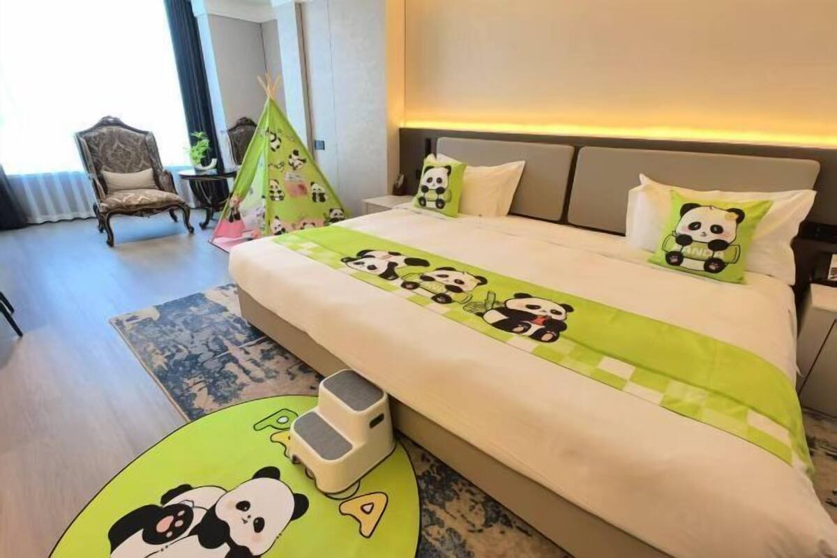 A hotel room with a bed, a chair, a small table, and a green area rug.
