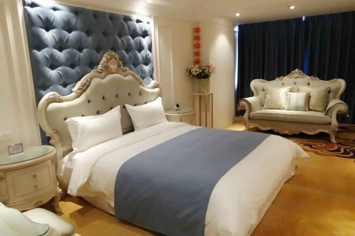 A luxurious bedroom with a large bed, a classic white and gold upholstered sofa, and a tufted headboard.