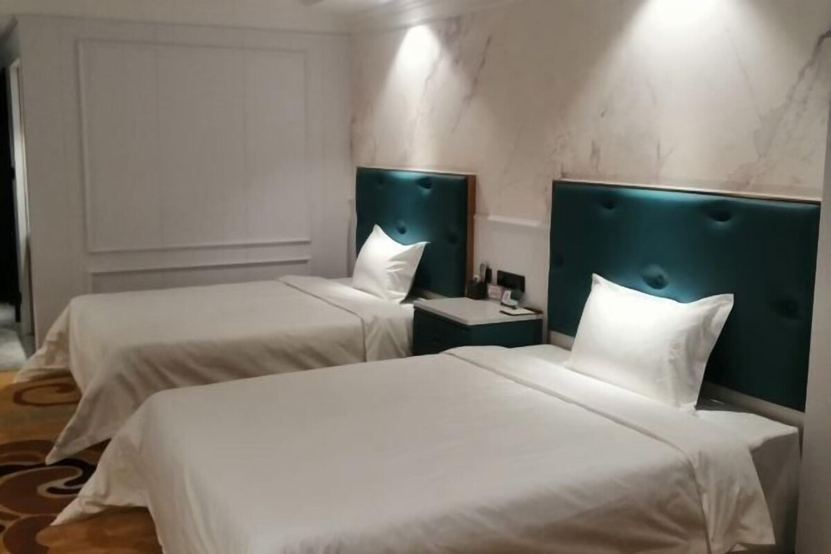 Habitació d'hotel amb dos llits individuals, cadascun amb un capçal blau cel, roba de llit blanca i una tauleta de nit amb una làmpada.
