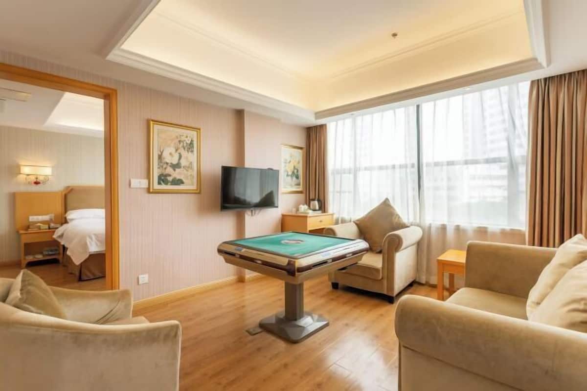A hotel room with a pool table, a sofa, a TV, and a large window with curtains.