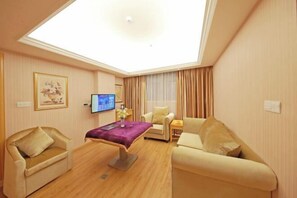 Una habitación de hotel con tragaluz, televisor de pantalla plana, sofá, sillón y una pequeña mesa.