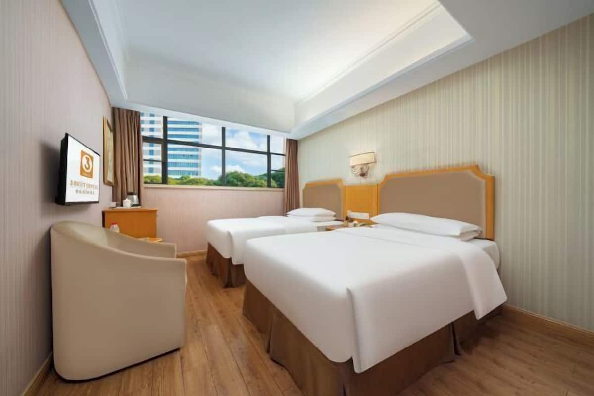 A hotel room with two beds, a sofa, a TV, and a window with a city view.
