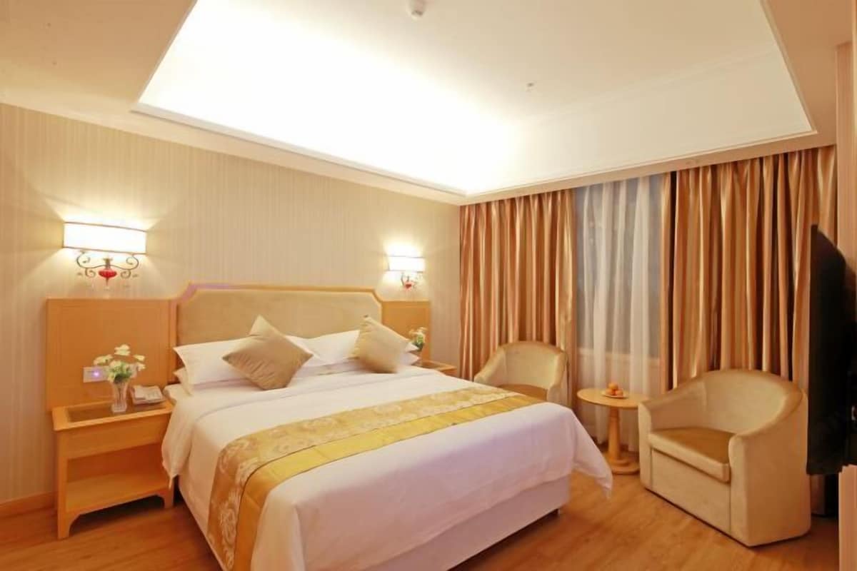 Una habitación de hotel con una cama grande, dos mesitas de noche, un televisor, una silla y una pequeña mesa.