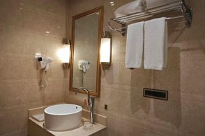 Un baño con un lavamanos redondo, un espejo, un perchero para toallas y dos luces fijadas a la pared.