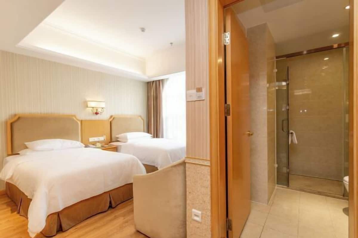 A hotel room with two beds, a shower, and a small seating area.