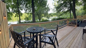 A wooden deck with a round table and chairs, overlooking a lake and surrounded by trees. - Waterfront Ranch on The Delaware River (Matamoras)
