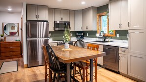 A modern kitchen with stainless steel appliances, wooden dining table, and light-colored cabinets. - Waterfront Ranch on The Delaware River (Matamoras)