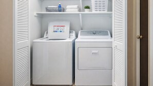 A laundry room with two stacked washing machines, a drying rack, and shelves with laundry baskets and a water bottle. - Waterfront Home, Stunning Canal Views, Deck (Navarre)