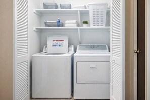 A laundry room with two stacked washing machines, a drying rack, and shelves with laundry baskets and a water bottle. - Waterfront Home, Stunning Canal Views, Deck (Navarre)