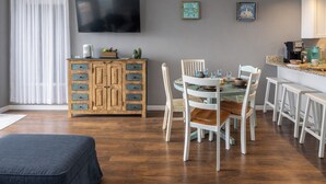A dining area with a round table, white chairs, a wooden cabinet, and a television mounted on the wall. - Waterfront Home, Stunning Canal Views, Deck (Navarre)
