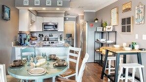 A kitchen with white cabinets, a microwave, and a refrigerator. There is a dining table with chairs and a small island with a sink. - Waterfront Home, Stunning Canal Views, Deck (Navarre)