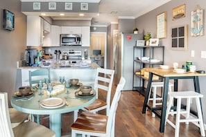 A kitchen with white cabinets, a microwave, and a refrigerator. There is a dining table with chairs and a small island with a sink.