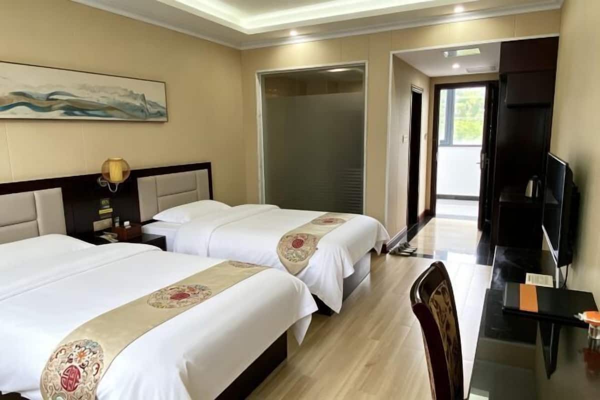 Une chambre d’hôtel avec deux lits, un bureau, une télévision et une porte coulissante donnant sur un balcon.