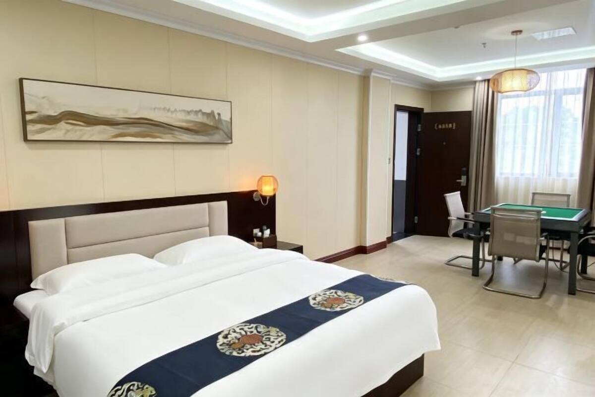 Une chambre d’hôtel avec un lit, un bureau sur lequel se trouve un billard vert, un tableau accroché au mur et un luminaire au plafond.