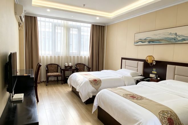 A hotel room with two beds, a desk, a chair, a TV, and a painting on the wall.