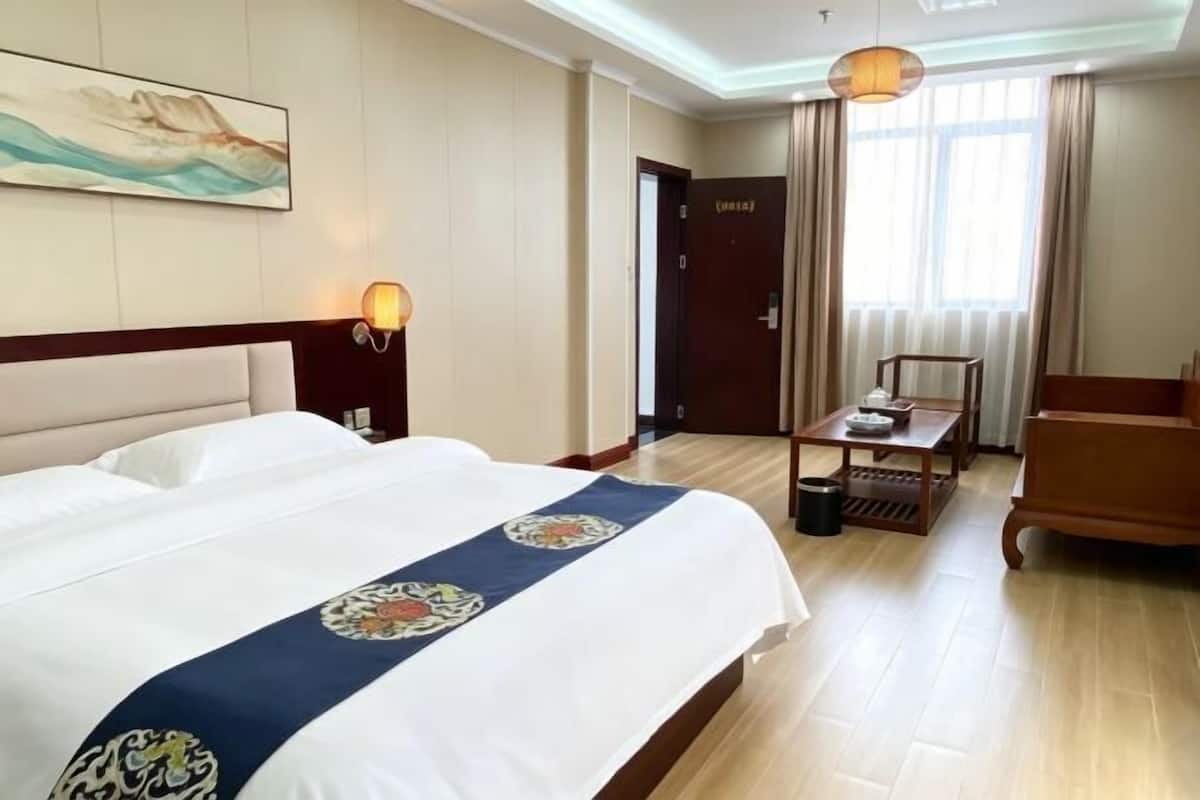 Une chambre d’hôtel avec un lit, un bureau, une chaise, une lampe et un tableau au mur.