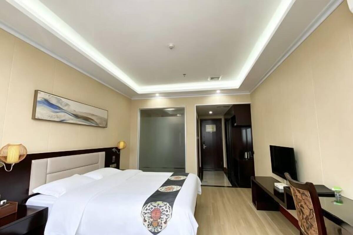Une chambre d’hôtel comprenant un lit, une table de chevet, une lampe, une télévision et une porte donnant sur une autre pièce.