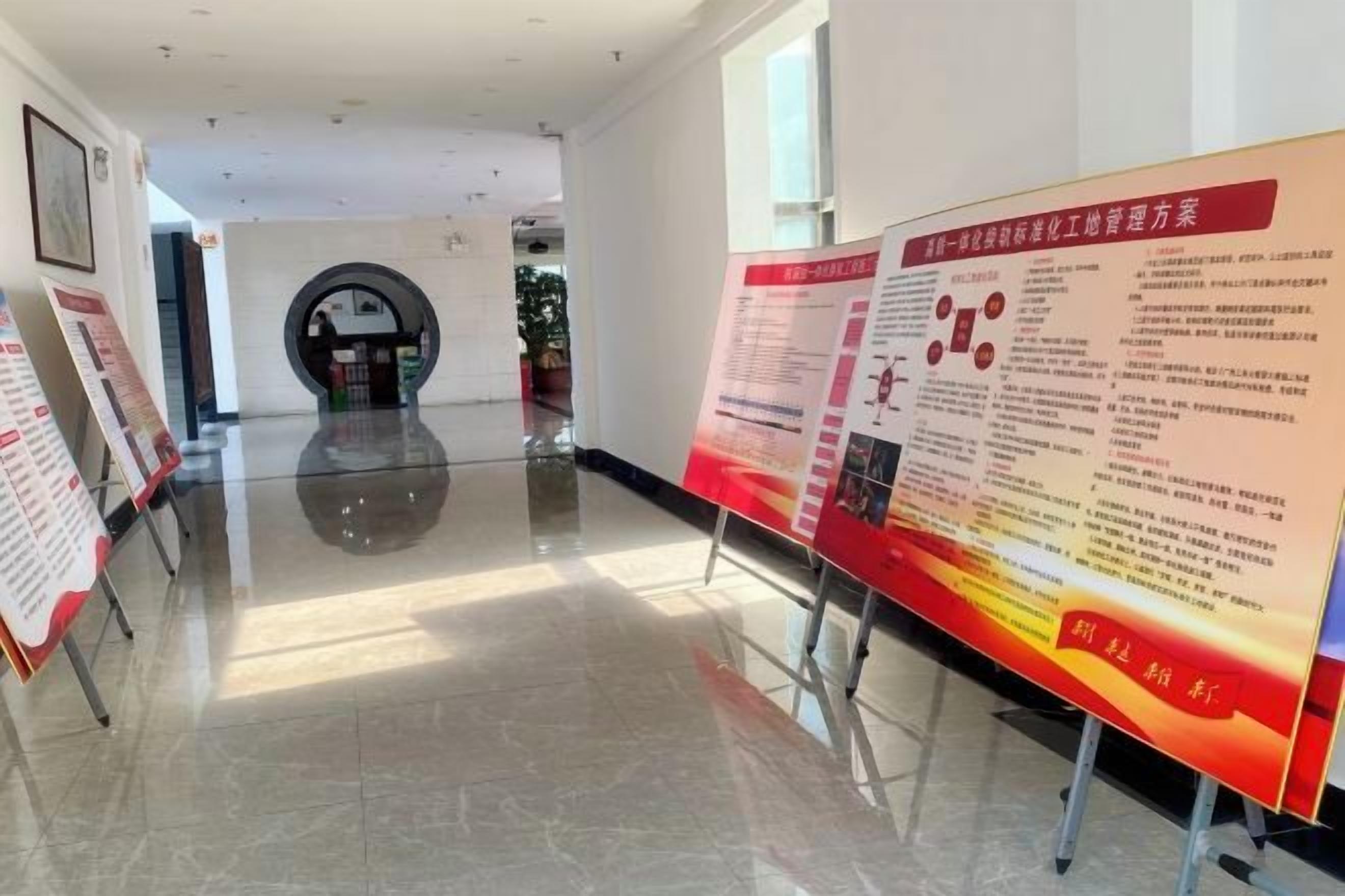 A corridor with informational posters on stands, a circular architectural feature in the distance, and a polished floor.