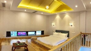 A bedroom with a bed, wooden floor, a small table with a vase, and a TV mounted on the wall. - Xile'er Hotel (Emeishan City)