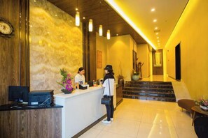 A hotel reception area with a marble wall, a reception desk, and a staircase leading to an upper floor. - Xile'er Hotel (Emeishan City)
