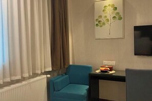 A room with a blue armchair, a small table with fruits, a framed artwork, and a TV on the wall. - Xile'er Hotel (Emeishan City)