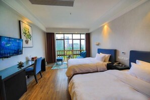 A hotel room with two beds, a desk, a TV, and a balcony with a view of buildings. - Xile'er Hotel (Emeishan City)