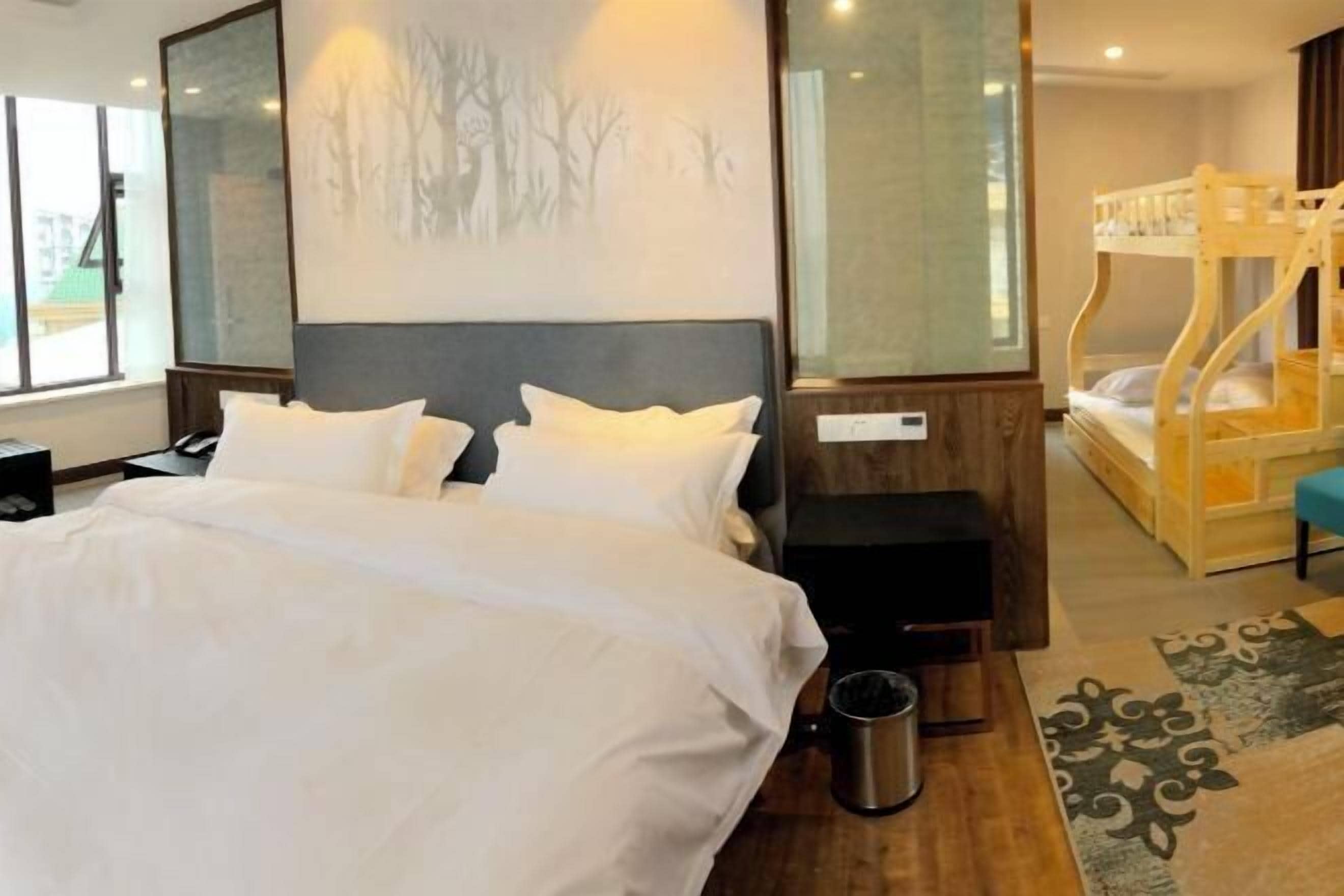 Een hotelkamer met een groot bed, een houten hoofdeinde, een stapelbed en uitzicht op bomen door het raam.
