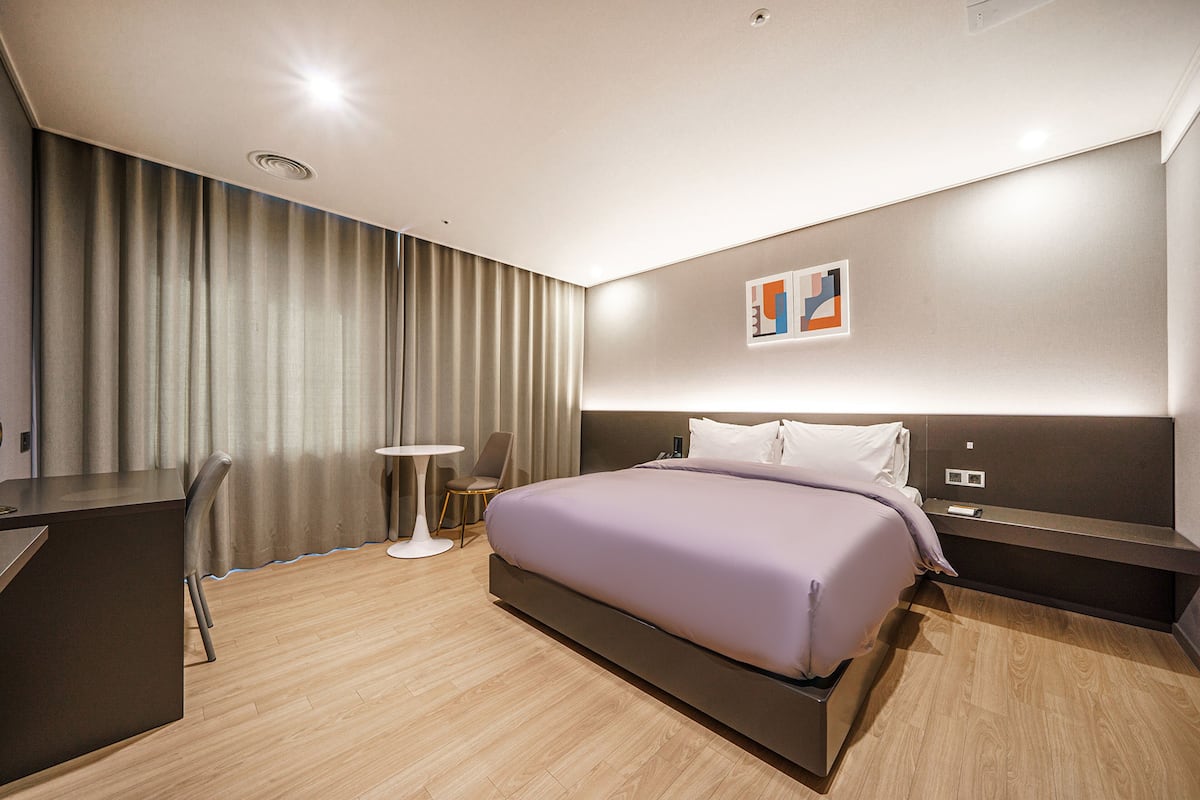 A modern hotel room with a large bed, a desk, and a chair.