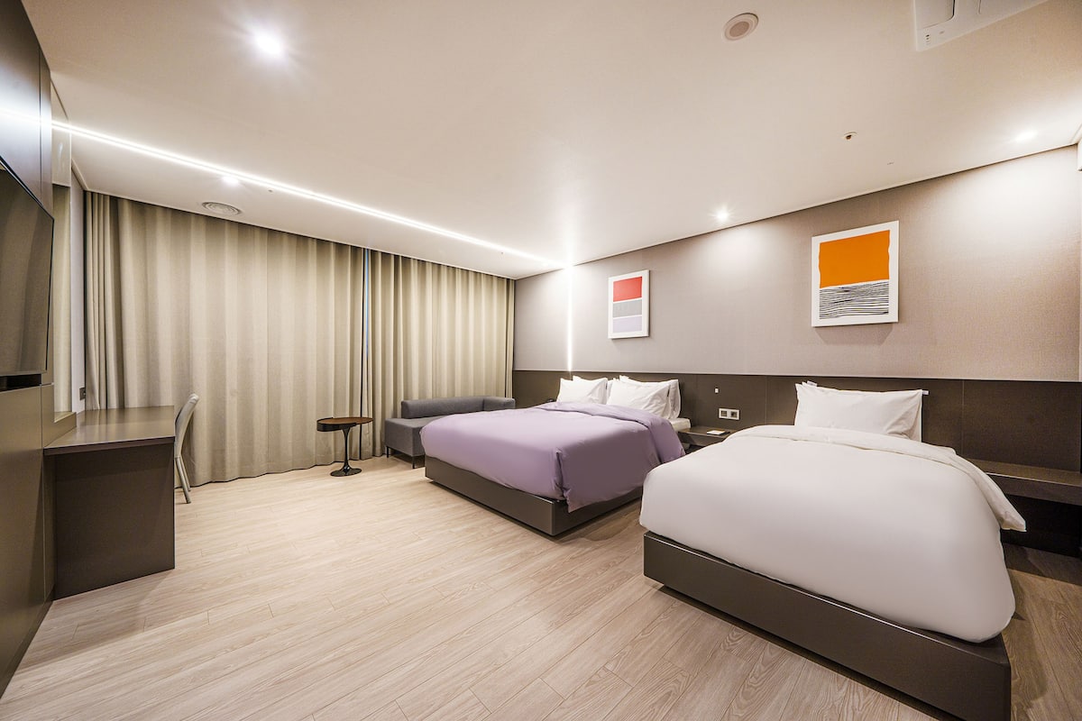 A modern hotel room with two beds, a desk, and a chair.