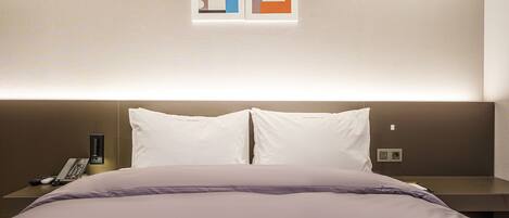 A hotel room with a bed, two pillows, a nightstand with a phone, and a wall-mounted artwork.